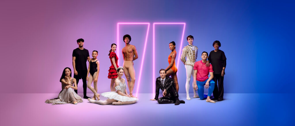 Group of dancers and creatives from English National Ballet standing and sitting against a gradient pink-to-blue background with two glowing neon rectangles. The group includes people in various ballet costumes, from classical tutus and tights to contemporary outfits and casual wear.