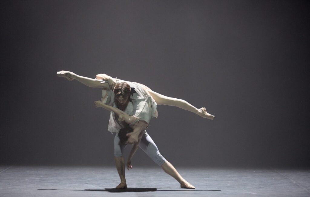 Two ballet dancers performing an intricate and dramatic lift during a pas de deux from Manon