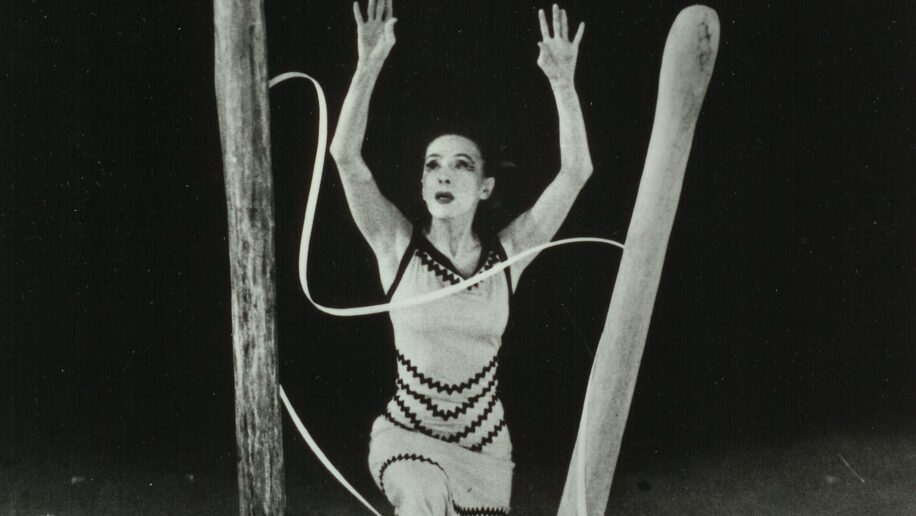 A dancer performs on stage surrounded by large wooden structures and long