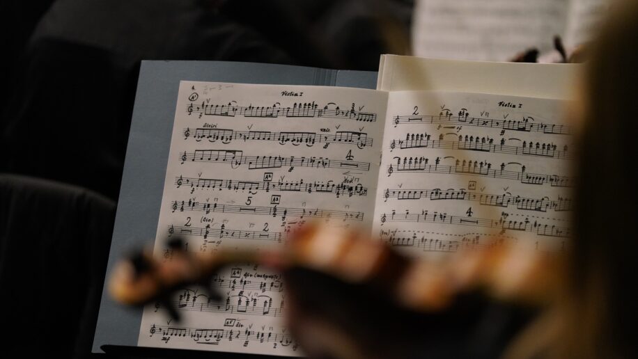 Close-up of a violinist’s music sheet during a performance or rehearsal, with handwritten notes and markings visible on the pages and a blurred violin in the foreground.