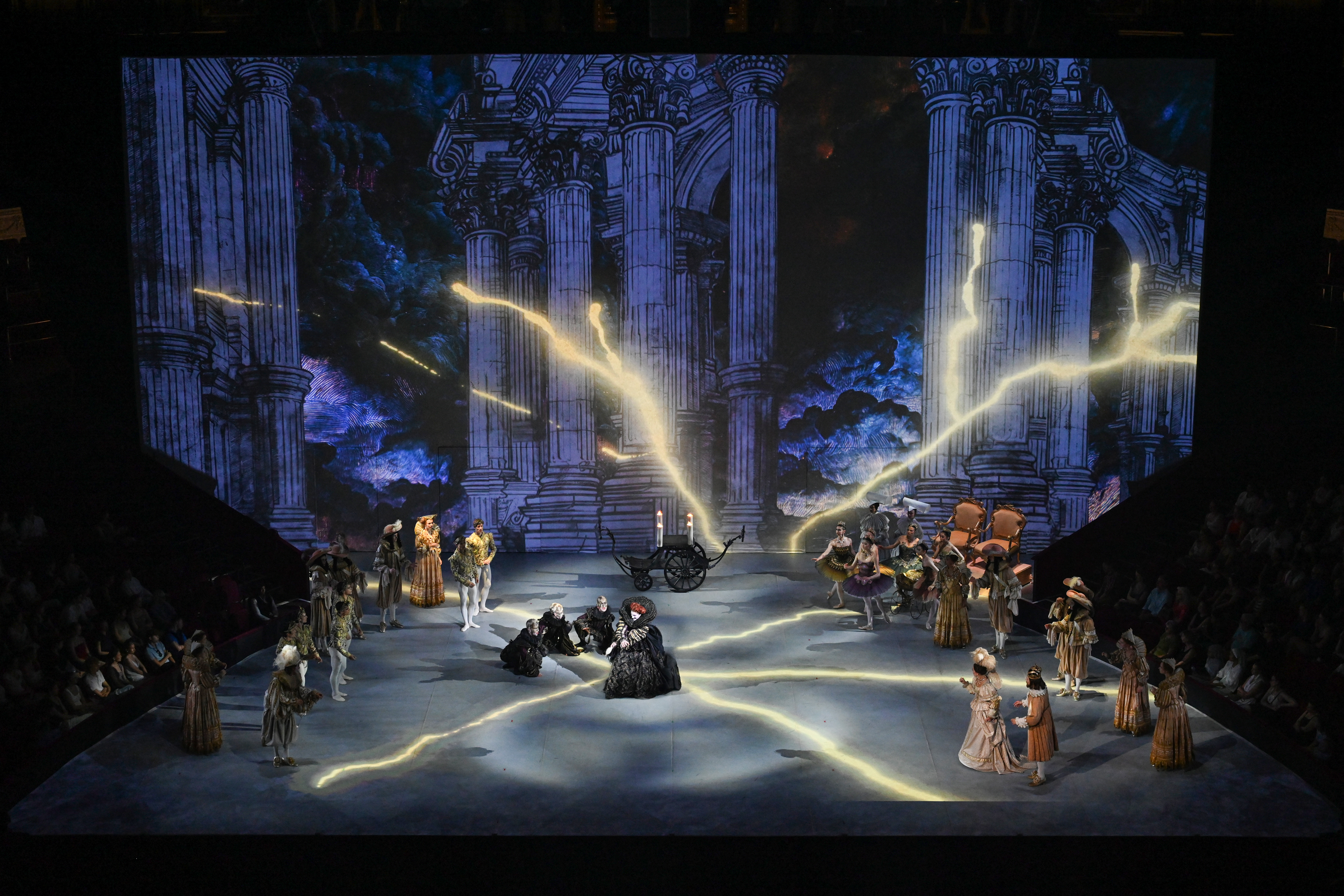 Overhead shot of dancers on stage, large lightening bolts of light across stage and a dark background with stone pillars