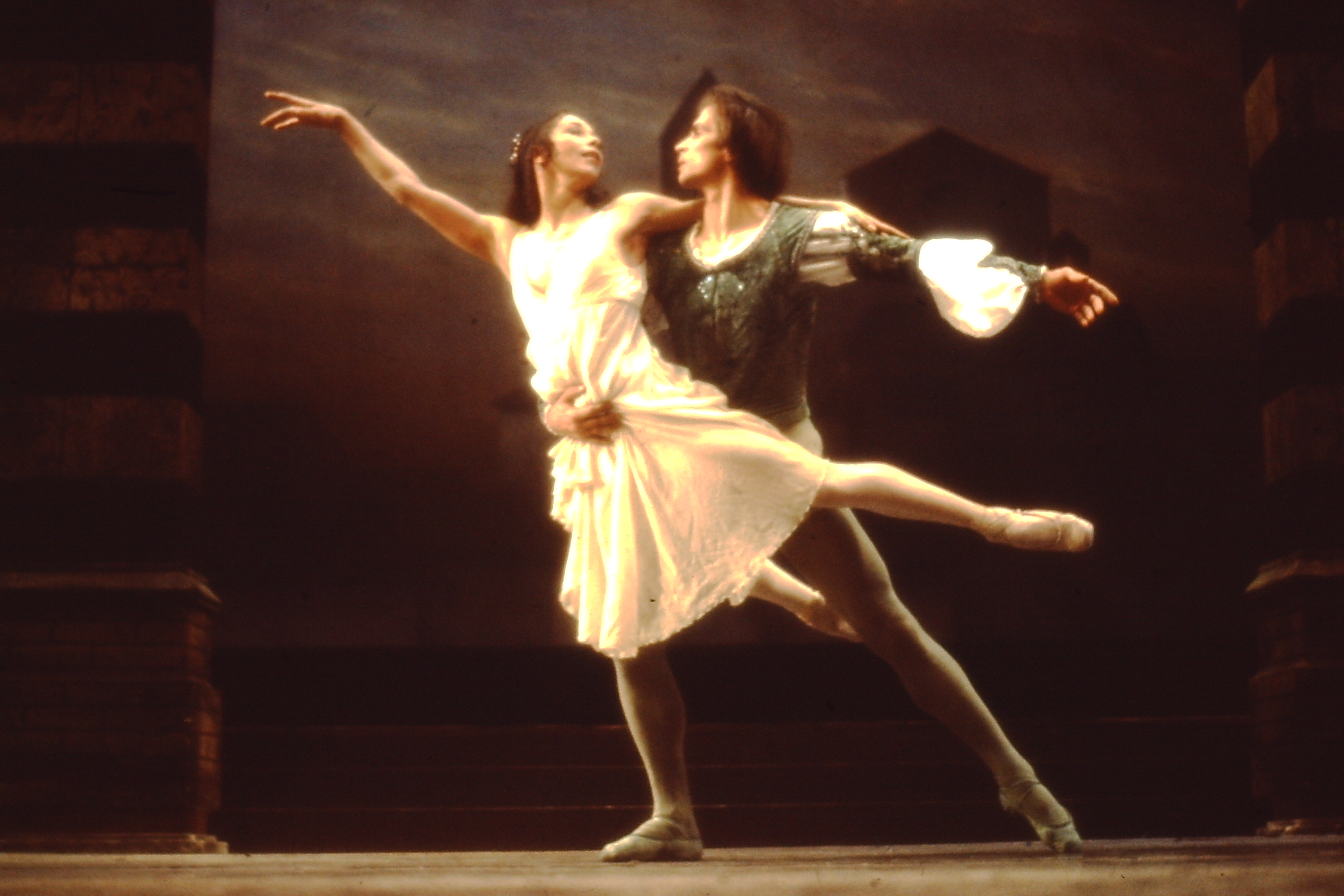 Two dancers on stage, male dancer holding the female dancer up who extends her hands and legs out entwined with his.