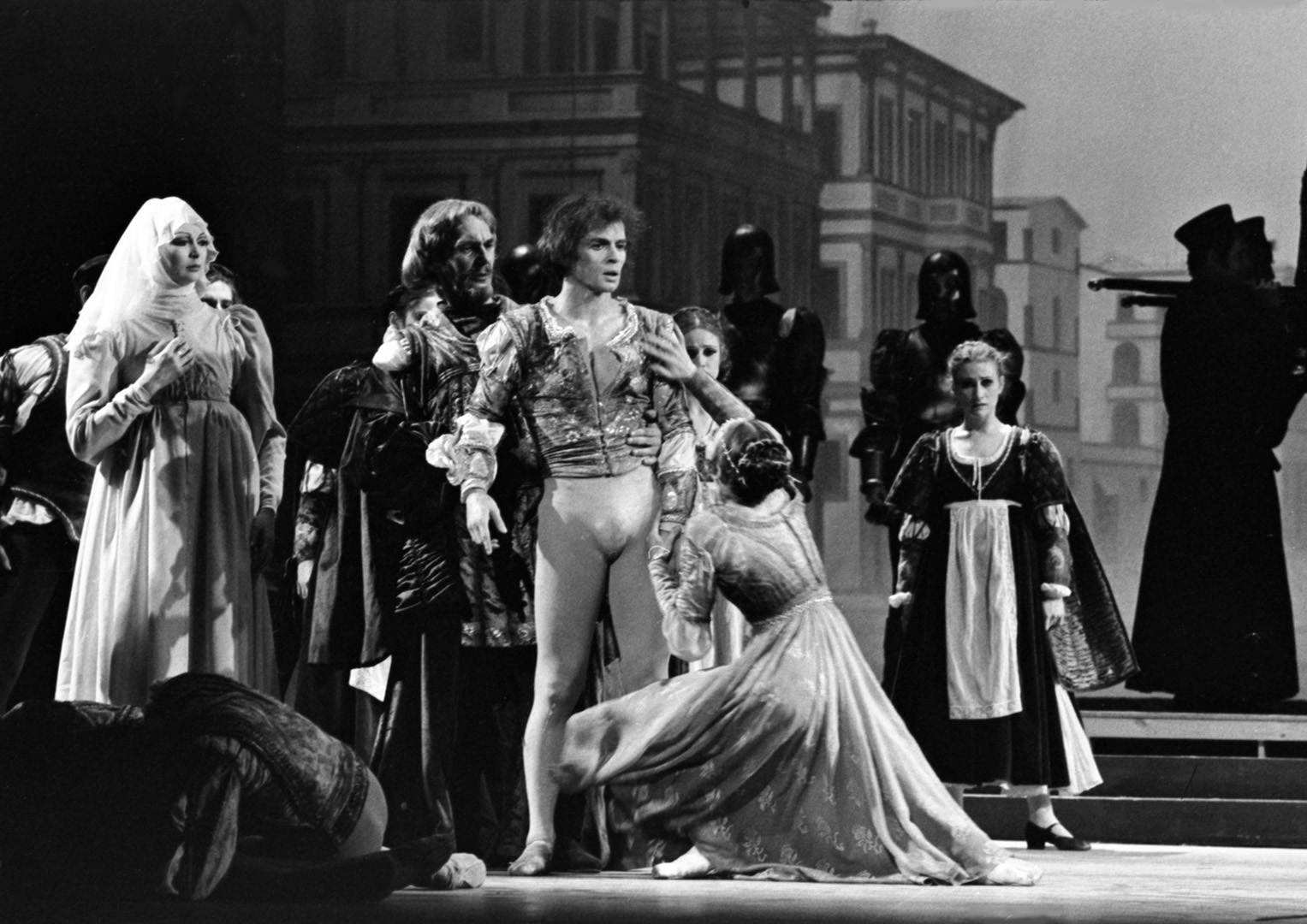 Dancers standing on stage, with one kneeling in tears in front of the others